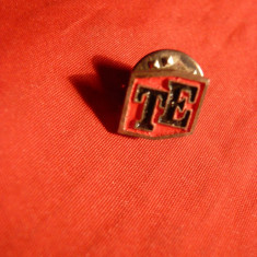 Insigna cu initialele TE pe fond rosu -metal argintat ,cu buton