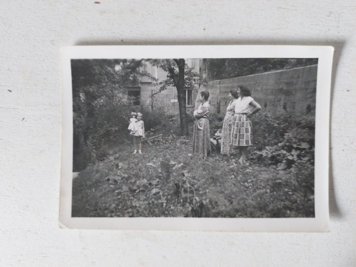 Fotografie veche anii 60, 3 femei si o fetita cu papusa in mana, intr-o curte, 9.5x6.5cm, alb-negru