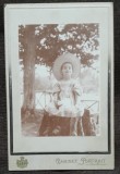 Fotografie pe carton, fetita la Slanic, asezata pe o bututuga, perioada interbelica