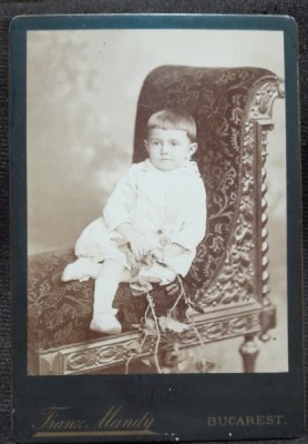 Fotografie pe carton, copil asezat intr-un jilt, inceput de secol XX foto