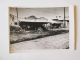Copie foto 177x124 mm cu un han de la periferie din anii 30,&icirc;n fundal se observă reclame la bere Luther și Vinuri