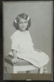 Fotografie pe carton, fetita cu fundite, stand pe scaun, inceput de secol XX