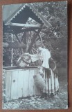 Fotografie tip carte postala, necirculata, tanara in port popular, sotand apa din fantana, inceput de secol XX