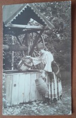 Fotografie tip carte postala, necirculata, tanara in port popular, sotand apa din fantana, inceput de secol XX