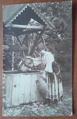 Fotografie tip carte postala, necirculata, tanara in port popular, sotand apa din fantana, inceput de secol XX foto