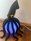 Lampă decorativă &icirc;n formă de calamar, realizată &icirc;n nuanțe de negru, alb și galben, cu lumină UV și alimentare prin USB.