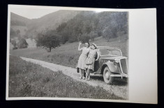 DOUA TINERE POZAND LANGA UN AUTOMOBIL DE EPOCA , PE UN DRUM DE TARA , INTRE DEALURI , FOTOGRAFIE TIP CARTE POSTALA , MONOCROMA, NECIRCULATA , DATATA foto