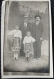 Fotografie tip Carte Postala, Doi barbati cu doi copii in costume traditionale romanesti, perioada interbelica
